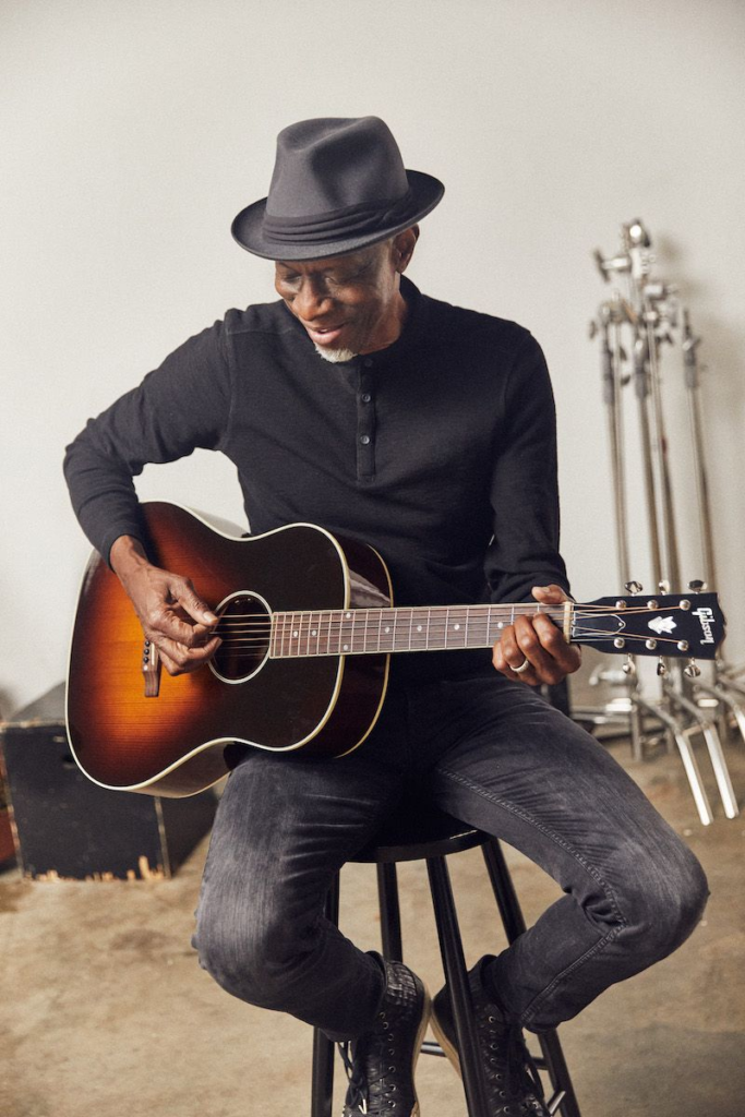 Pop Hombre mayor vestido de negro tocando una guitarra acústica Gibson.