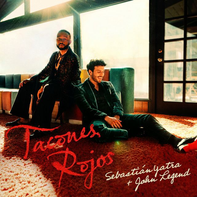 Sebastián Yatra y John Legend sentados en una sala, promocionando su canción "Tacones Rojos"